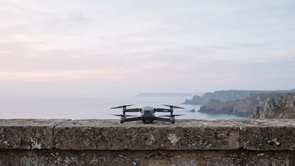 Un piccolo drone appoggiato su un parapetto di pietra davanti a un ampio cielo mattutino e a una costa lontana